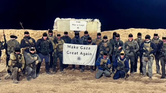 Una fotografía de un grupo de hombres con uniformes de estilo militar y armas, con la cara parcialmente oculta por barras negras, posando ante un fondo desértico. Llevan una pancarta con el logotipo de la empresa de Josh Miller y el lema 