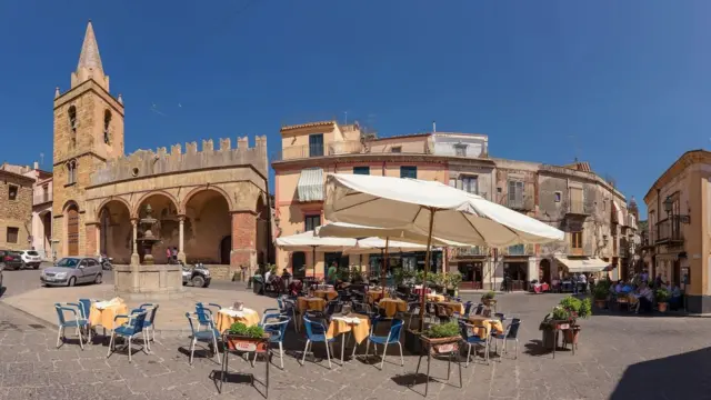 Una plaza con sillas, mesas y sombrillas.