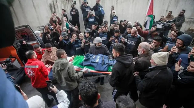 Un grupo de personas, algunos de ellos con chalecos azules que dicen PRENSA reunidas viendo como sacaban a Shatha al-Sabbagh en una camilla