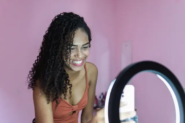 Una mujer joven sonriente se prepara para hacer una grabación de video con un iPhone y una luz circular.