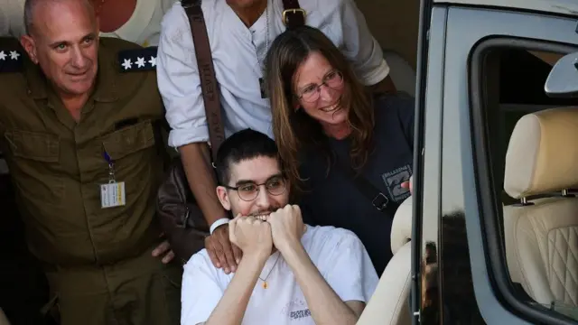 El rehén liberado Evyatar David, sonríe con los puños junto a la boca y mira desde el interior de un helicóptero. Junto a él, una mujer y un militar también sonríen.