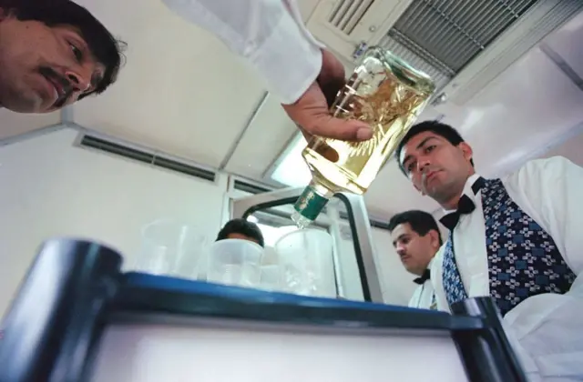 Un camarero sirve un trago de tequila a abordo del tequila exprés ante la mirada de otro.