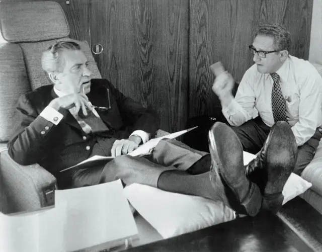 Richard Nixon (izq.), recostado en un asiento del avión presidencial, discutiendo con Henry Kissinger (der.)