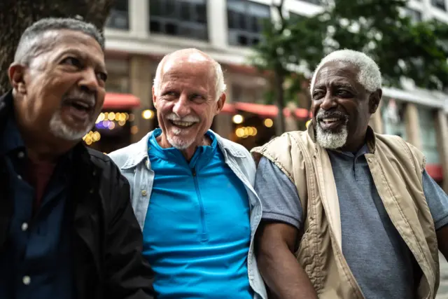 Tres amigos de edad madura, sonrientes, sentados en un sitio público