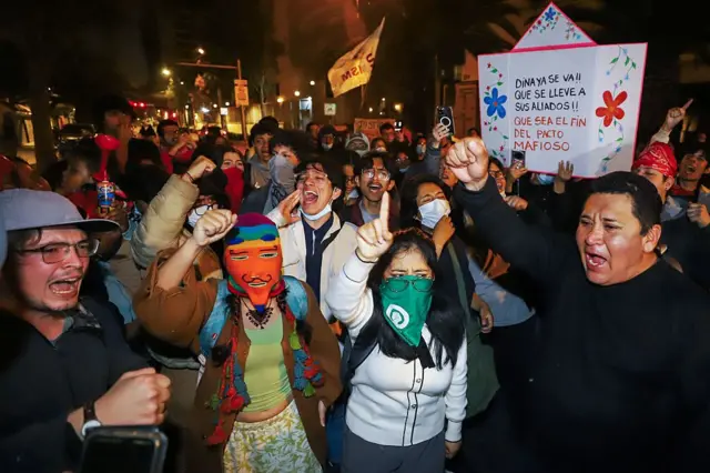 Manifestantes participan en una protesta contra la expresidenta. Es un grupo nutrido de gente, algunos con sus caras tapadas con máscaras, pañuelos o mascarillas, protestan con el brazo derecho en alto con el puño cerrado y carteles donde se lee