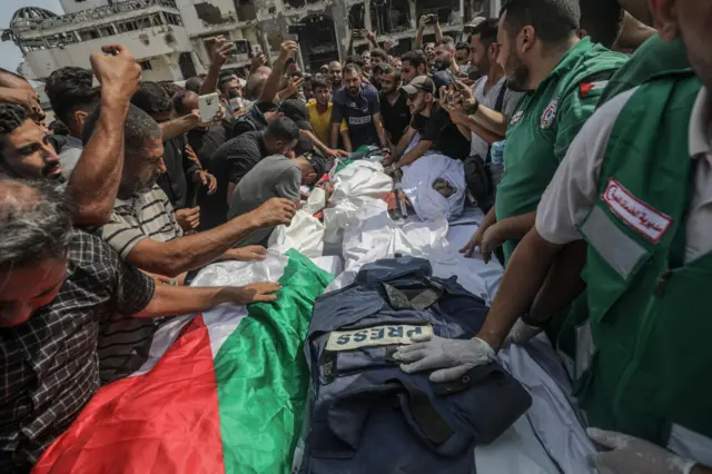 Una multitud rodea los cuerpos de los reporteros muertos en el ataque israelí, que están cubiertos por la bandera palestina y un chaleco antibalas en el que se lee 