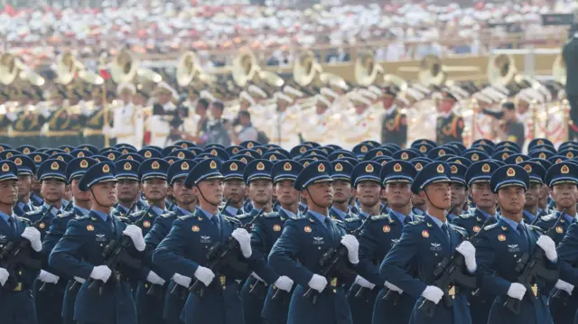 Soldados chinos con uniforme azul desfilan armados en formación.