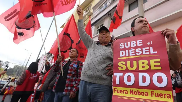 Manifestantes gritan consignas mientras sostienen un cartel que dice: 