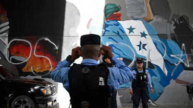 imagen de dos policías frente a un mural que tiene la bandera de Honduras 