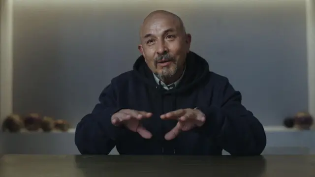 César Fierro sentado durante una entrevista del documental La Libertad del Fierro d2024. Está calvo y tiene barba canosa. Mueve las manos al hablar. 