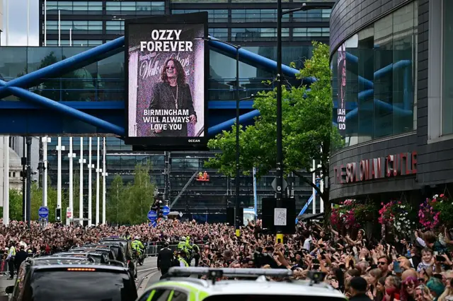 Las calles de Birmingham llenas de gente despidiendo a Ozzy, mientras que en el fondo se lee un letrero que dice 