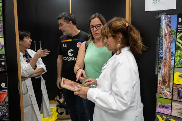 Marisa Vázquez, con bata blanca, recoge una fotografía que le entrega una mujer con camiseta verde ante otros miembros del equipo.