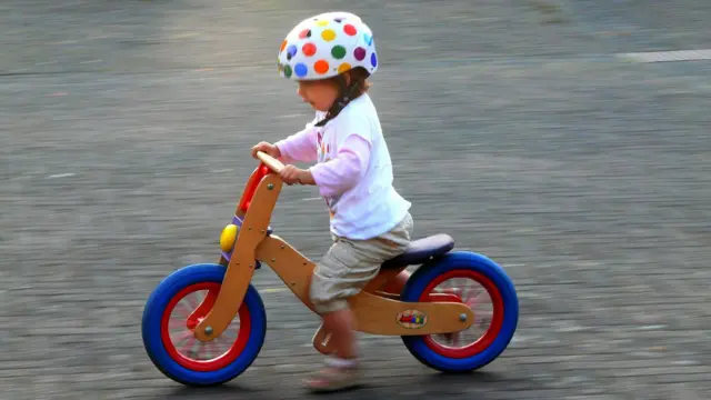 Un niño montando una bicicleta de madera. 