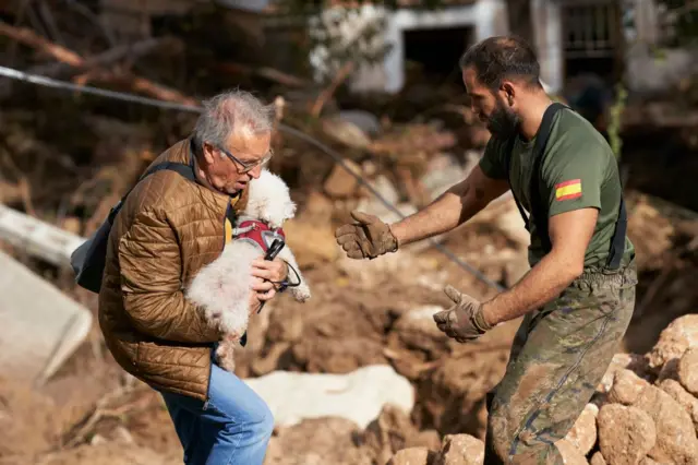 Un hombre y un perro afectados por las riadas ayudado por un militar. 