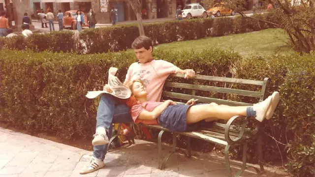 Sobre un asiento en lo que parece ser una plaza, Willem está sentado con las piernas cruzadas y lee el periódico. En su regazo, Annette posa su cabeza con los ojos cerrados.