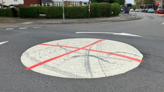 Una rotonda blanca en medio de Brandwood Road y Woodthorpe Road en Birmingham; fue vandalizada con pintura en aerosol roja para que parezca una bandera inglesa con la cruz de San Jorge.