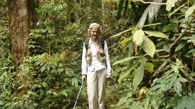 Annette lleva ropa ligera, una mochila y un palo para montañismo. Está rodeada de una exuberante vegetación.