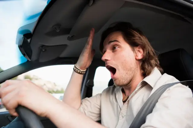 Un hombre hace un gesto de haber olvidado algo mientras conduce un auto.