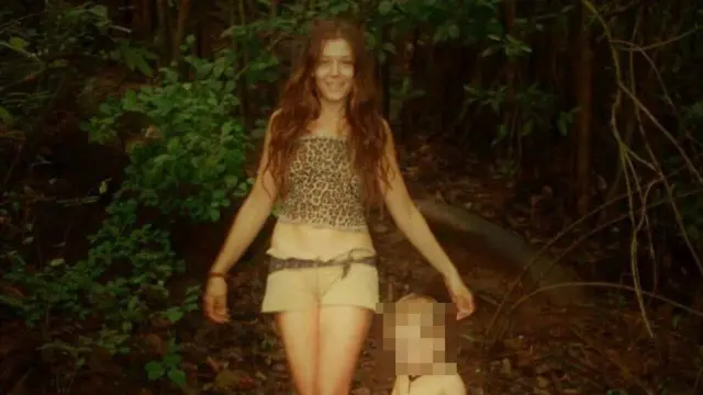 Nina Kutina, sonriente, con melena larga oscura, pantalones cortos y una camiseta con estampado de leopardo, posa en un sendero en la selva con un niño de unos cuatro años.