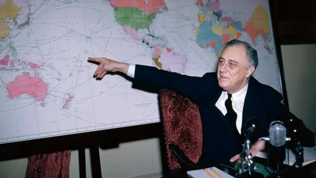 Roosevelt sentado en una silla apuntando a un mapa