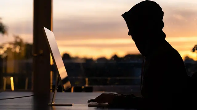 Un hombre con la cara cubierta mirando una laptop
