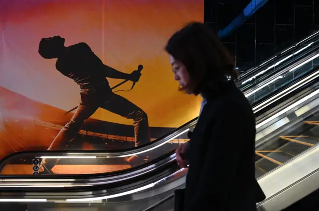 Una mujer sube por una escalera mecánica pasando junto a un cartel de la película Bohemian Rhapsody en un cine de Pekín el 27 de marzo de 2019.