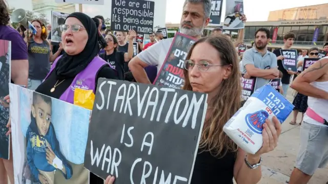 Personas en Tel Aviv con bolsas de comida simbólicas. Llevan pancartas con imágenes de niños en estado de desnutrición y un cartel que dice