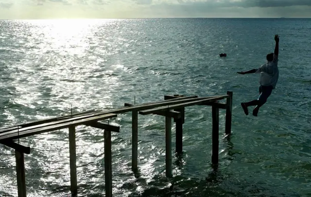 Hombre lanzandose desde un muelle cubierto de agua.