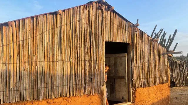 Una joven wayuu parada en la puerta de una casa tradicional.