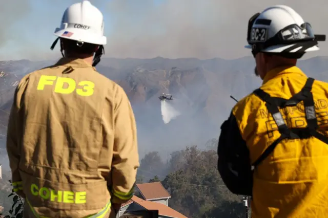 Bomberos ven como un helicóptero arroja agua a un foco de incendio