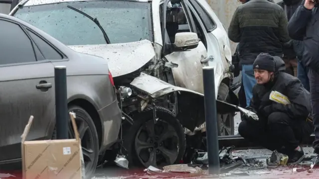 Una persona observa de cerca el carro blanco que sufrió daños por la explosión. 