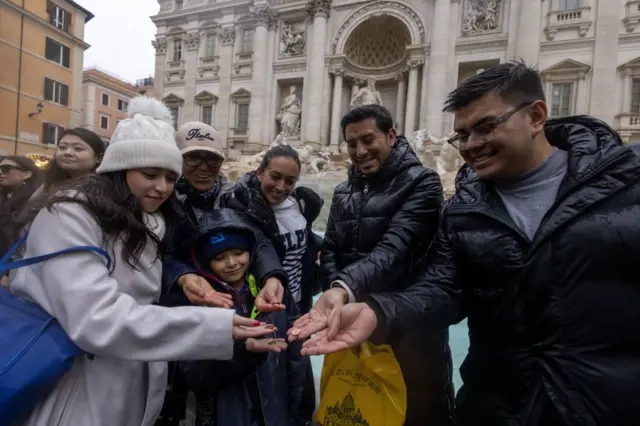 Un grupo de personas muestra las monedas que va a lanzar a la Fontana di Trevi.