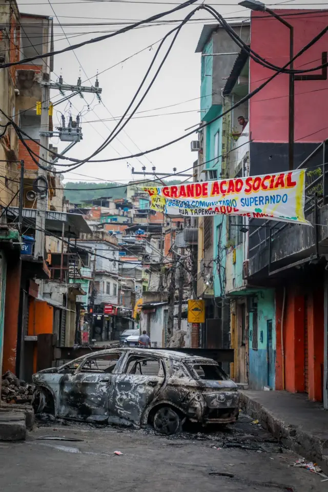 Un coche quemado bloquea el paso en una favela.