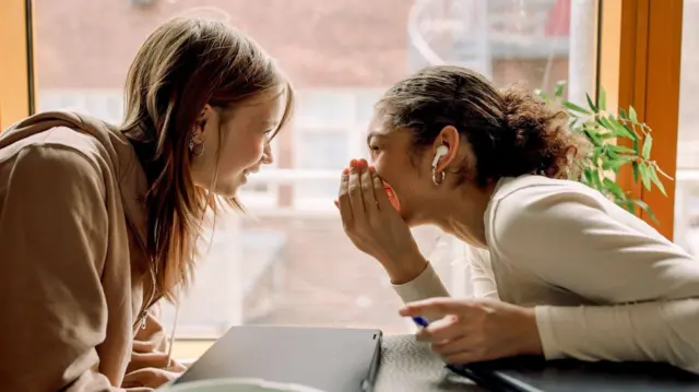 Dos mujeres jóvenes estaban sentadas una frente a la otra en una mesa, chismorreando y riendo.