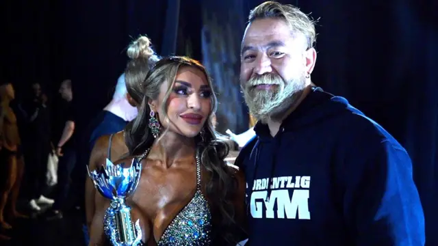 Roya Karimi sostiene un trofeo mientras mira con admiración a su esposo, Kamal Jalaluddin, que sonríe a su lado.