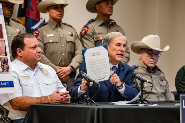 El zar fronterizo de Texas, Mike Banks, izquierda, y el director del Departamento de Seguridad Pública de Texas, Steve McCraw, derecha, observan cómo el gobernador Greg Abbott firma una proclamación que declara a la pandilla venezolana Tren de Aragua (TdA) una organización terrorista internacional.