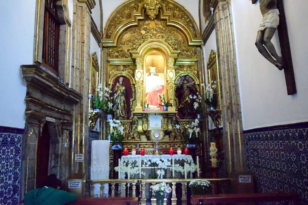 Altar de la iglesia más pequeña de la CDMX con tres figuras y flores.