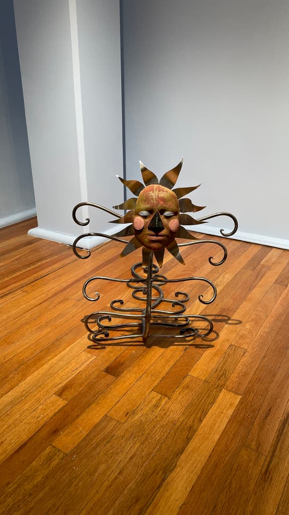 Escultura de metal en forma de gusano con cabeza de máscara.