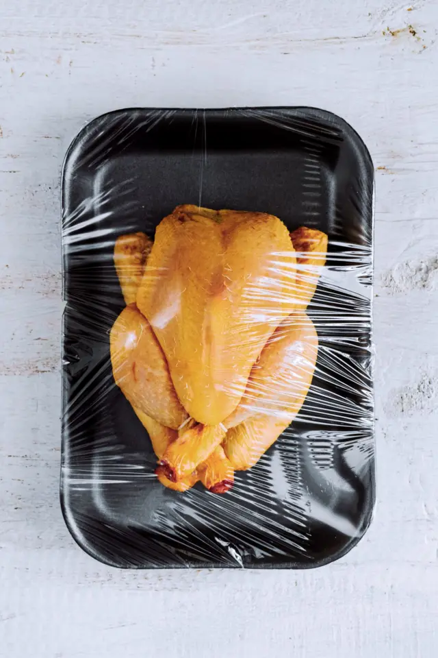 Un pollo en una bandeja plástica con envoltura plástica alrededor.