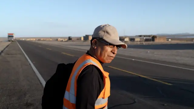 Ruben mira a un lado de la carrtera antes de atravesarla. Al fondo está el pueblo.