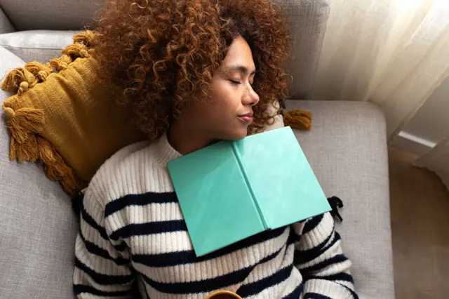 Una mujer durmiendo con un libro en su cuello.