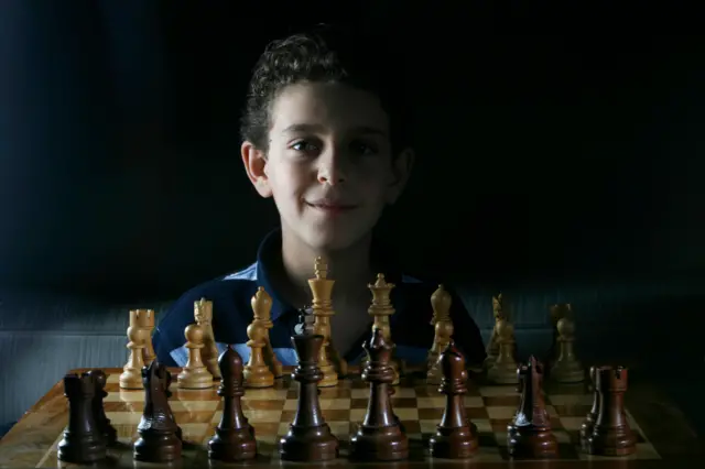 Un joven Daniel Naroditsky sentado detrás de un tablero de ajedrez.