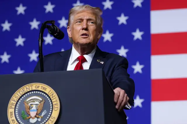Donald Trump, de traje, habla desde un atril con la bandera de Estados Unidos de fondo. 