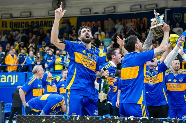 Sebastián Vega celebra la copa con su brazo derecho en alto, mientras que con su mano izquierda sostiene una botella de champaña, rodeado de sus compañeros