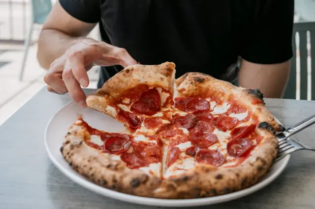 Primer plano de un hombre irreconocible comiendo pizza de pepperoni al aire libre en un restaurante