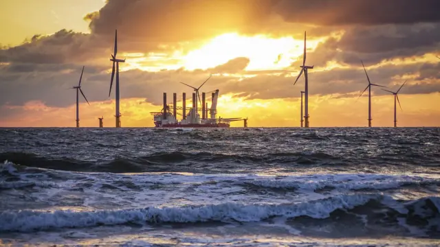 Vista de un parque eólico marítimo con un barco atravesándolo.