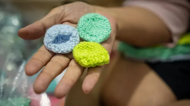 Tres pequeños gorros tejidos, sobre la palma de una mano.