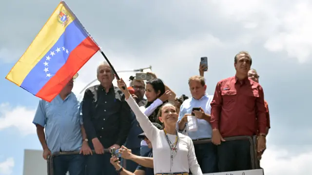 Machado ondea una bandera venezolana y sonríe.