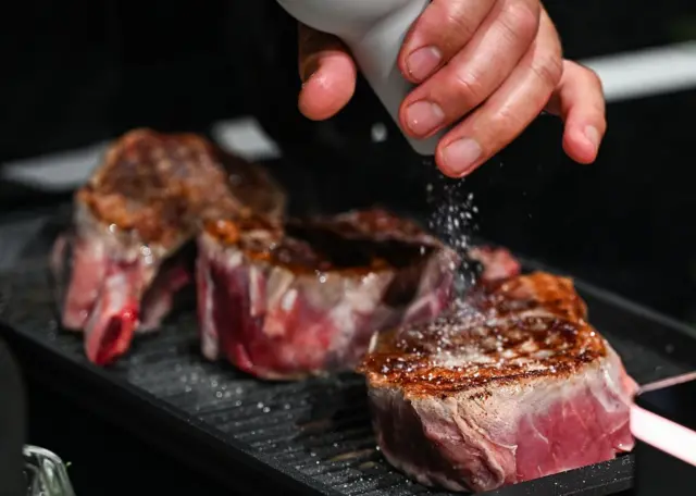 Mano agregando sal a un trozo de carne.
