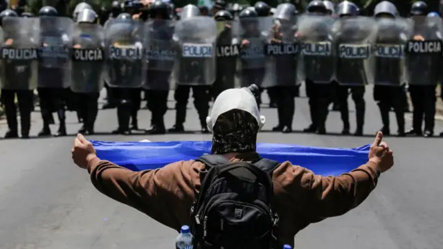 Un manifestante enmascarado muestra una bandera nicaragüense a un grupo de policías antidisturbios el 16 de septiembre de 2018.